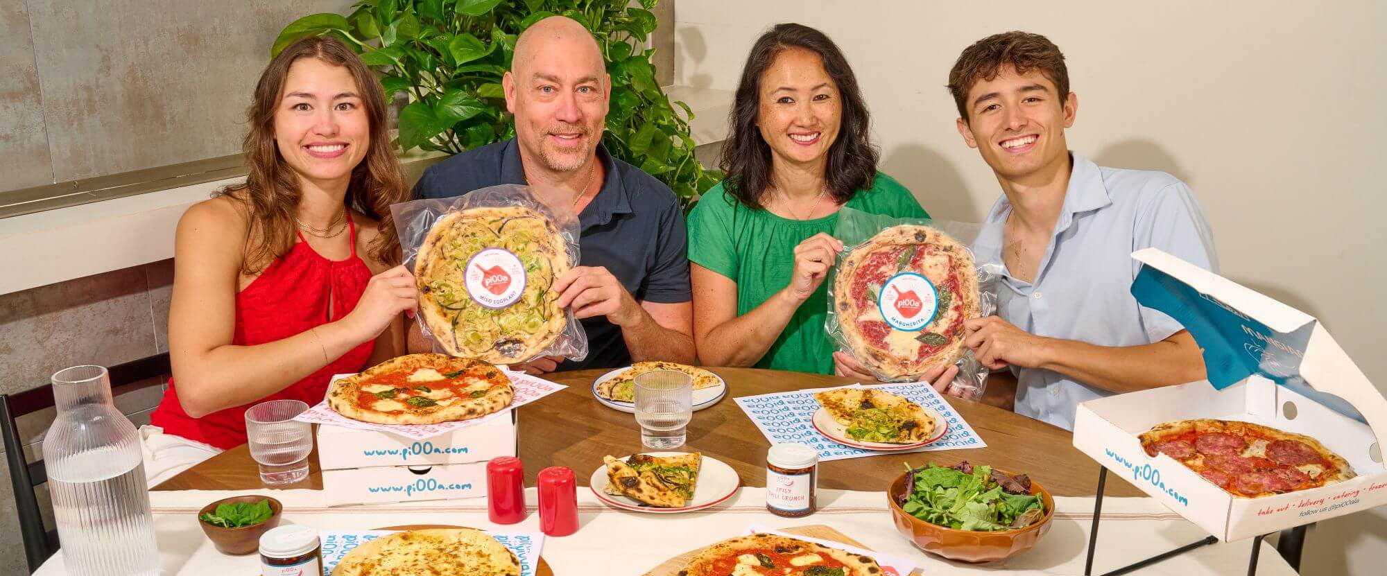 Family of four enjoying a pi00a meal together at a table with various pi00a and drinks.